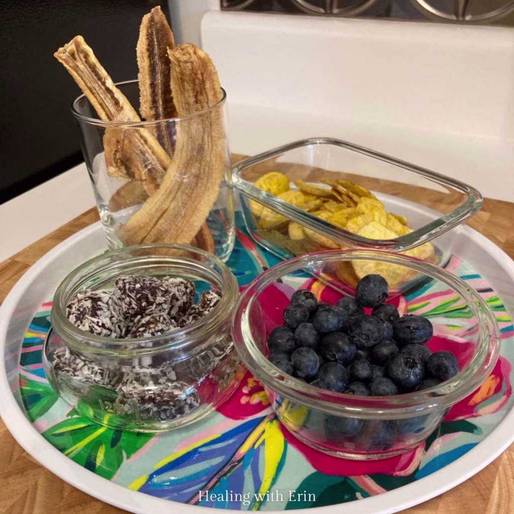 Tray of AIP compliant snacks including dried banana strips, plantain chips, coconut date rolls and fresh blueberries