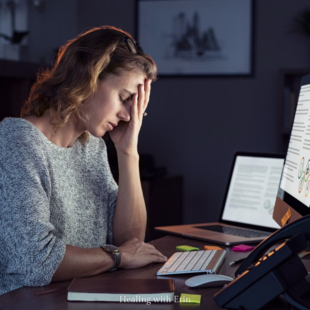 Woman sitting stressed at a computer in the dark late at night, researching elimination diets and autoimmune healing